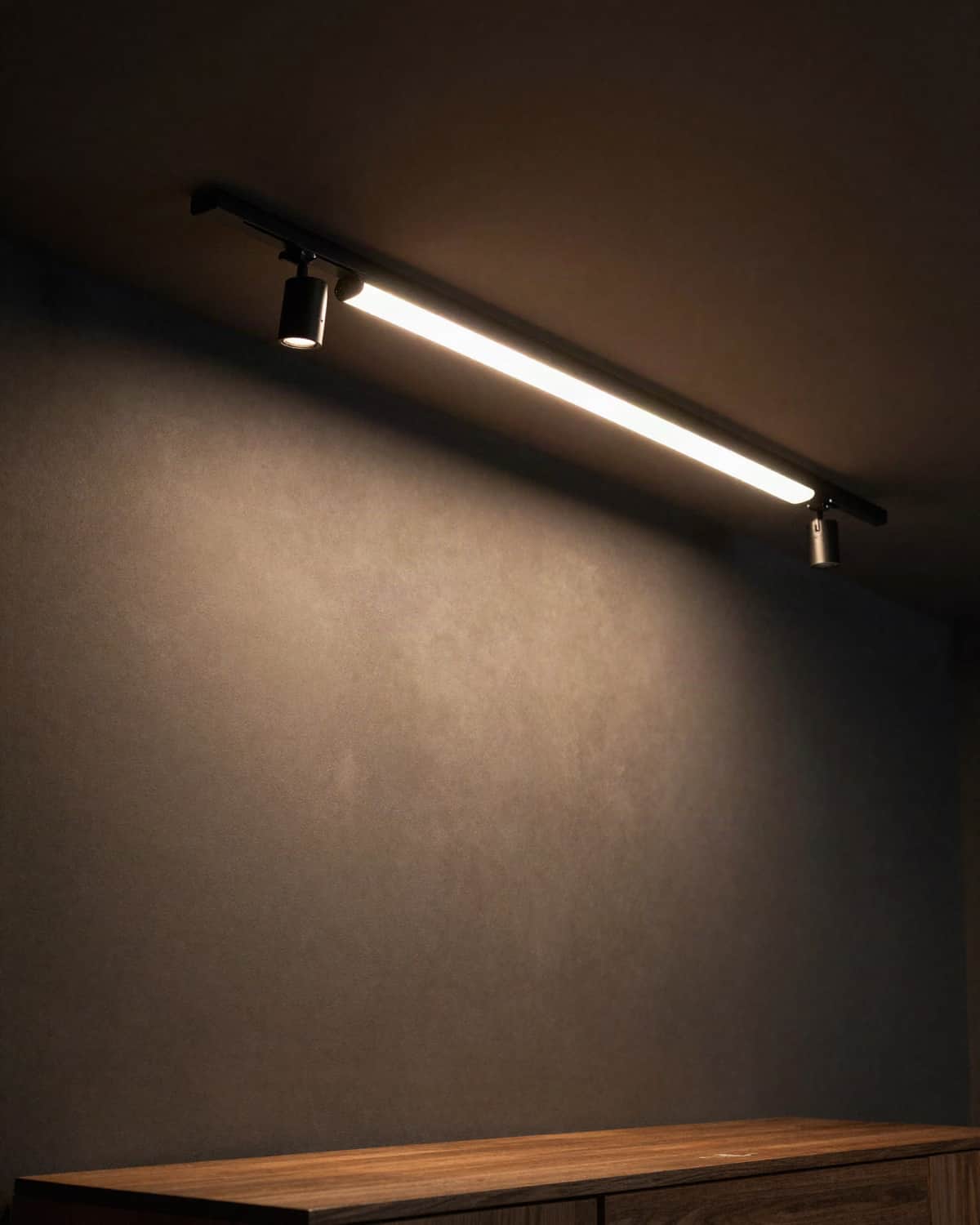 A matte-black magnetic track rail with a linear LED module and small spotlights washing a dark wall above a walnut sideboard