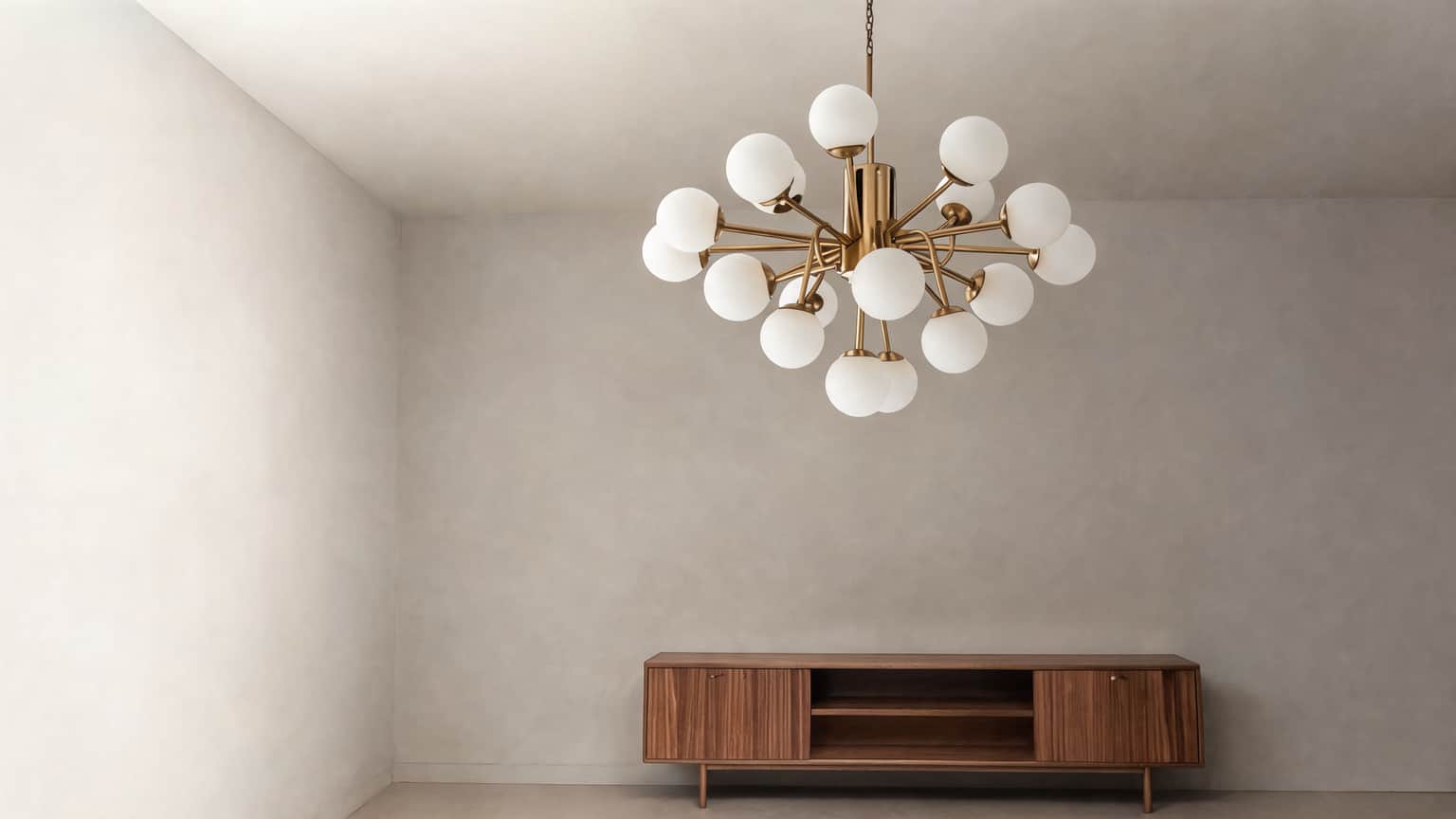 The same room in daylight: a modern brass chandelier of frosted glass globes, switched off and completely unlit, hanging above a walnut sideboard in a light, airy living room filled with soft natural light